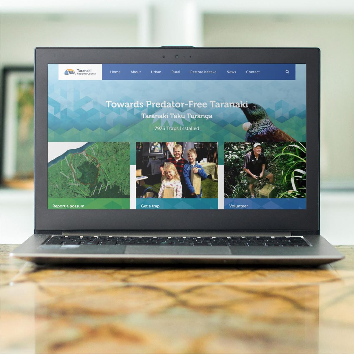 Laptop sitting on a desk with a screenshot of the Predator Free Taranaki website