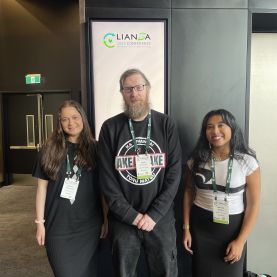 Wainui Witika-Park, Chris Cormack, and Aleisha Amohia at LIANZA 2025. They stand together smiling, wearing presenter lanyards