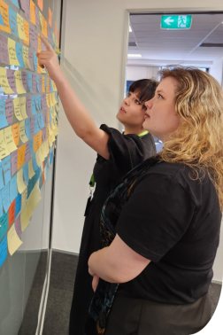 Maria and Fyfa read notes off a wall of brightly coloured post it notes.