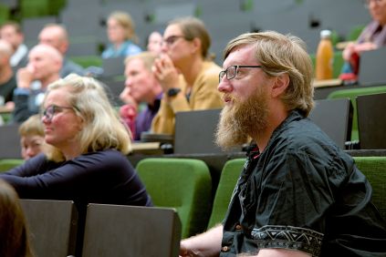 Chris Cormack sits in a lecture theatre. He's wearing glasses and has a beard.