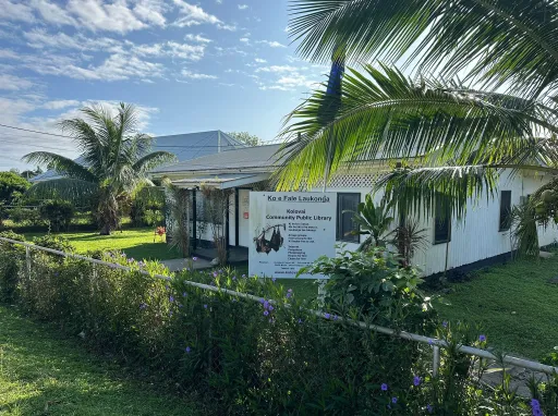 Photo of the Kolovai Community Public Library. In front of the library is a welcome sign display ‘Ko e Fale Laukonga’ with information about what’s available.  