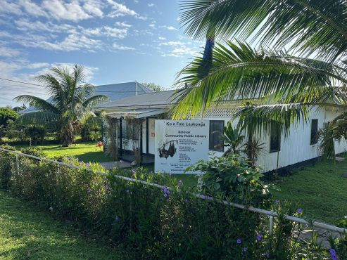 Photo of the Kolovai Community Public Library. In front of the library is a welcome sign display ‘Ko e Fale Laukonga’ with information about what’s available.  