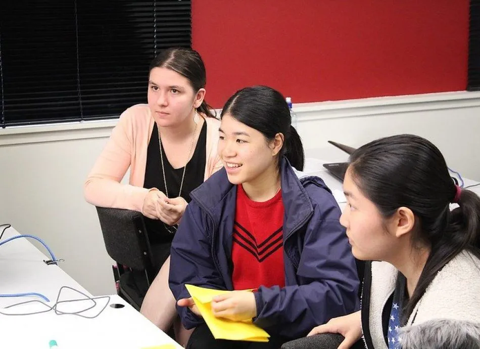 Three students are looking off camera towards a computer screen or instructor