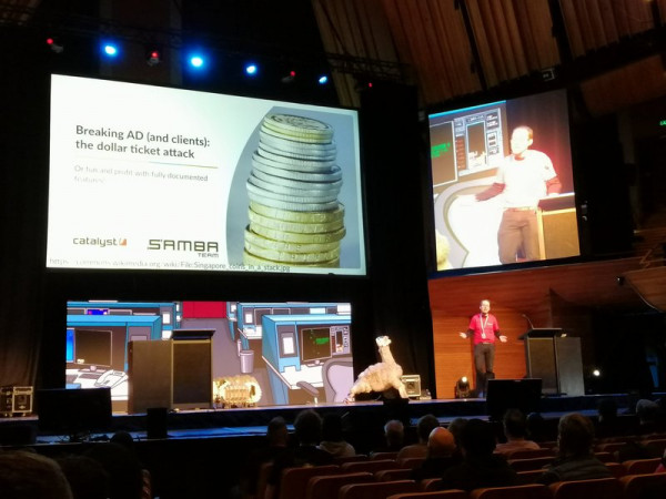 Andrew Barlett on stage giving a talk at Kawaiicon with big screens behind him.