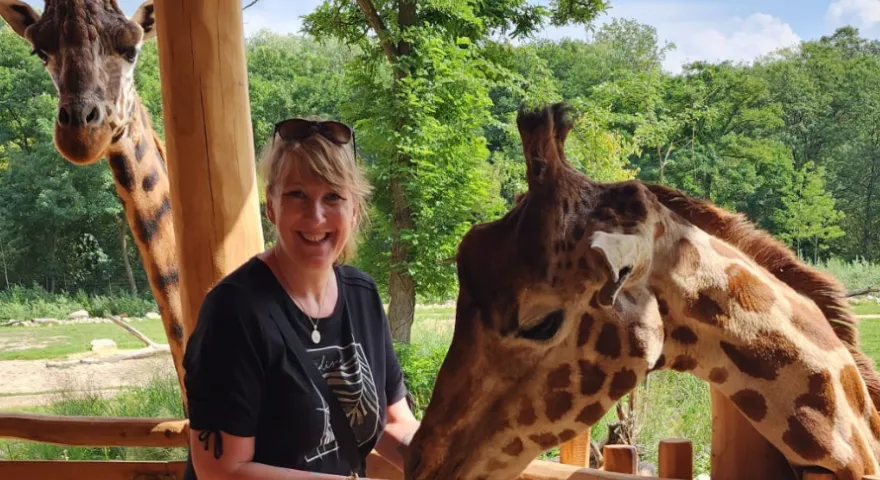 Alex Virtue zookeeper stands next to giraffes infront of a tree