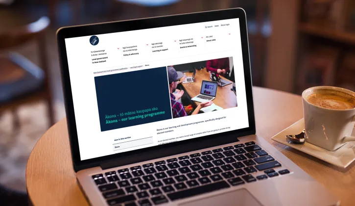 Open laptop displays the LGNZ website showing the landing page for Ākona, the digital learning platform for elected members. Next to the laptop is a flat white.