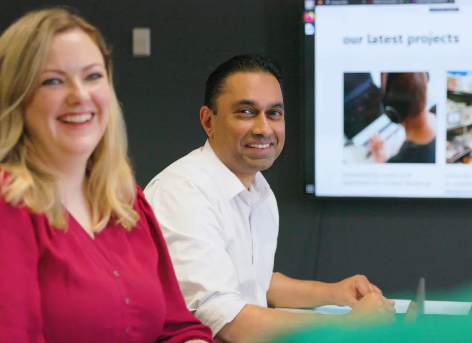 a man and woman sat infront of a screen with a website on it. They are both smiling