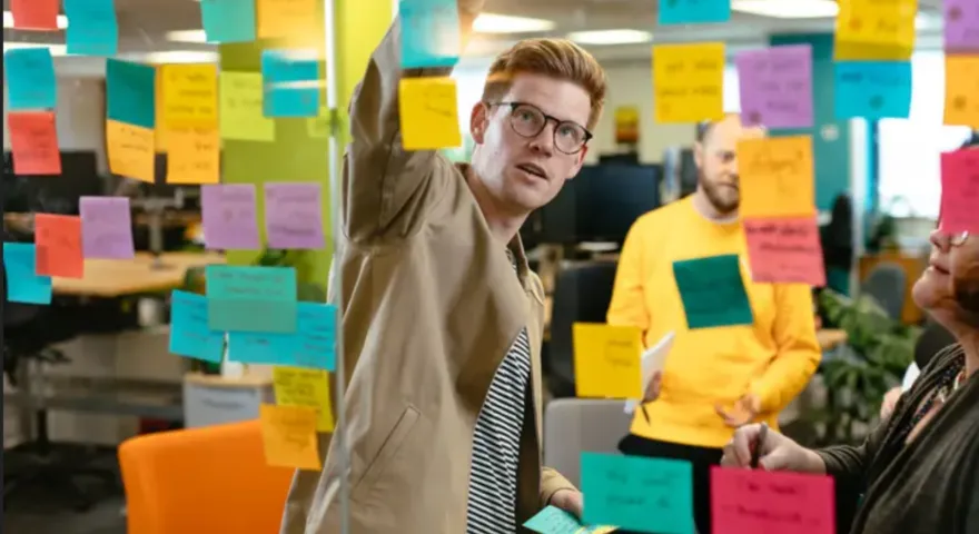 A man with glasses organising colourful Post-its on a glass board