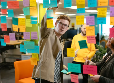 Dan van Ammers reaches up to place a post it note on a wall of post it notes. He has ginger hair and is wearing glasses