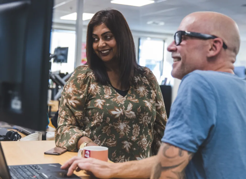 A woman with black hair and a man with a bald head and glasses smiling at their work on a computer screen