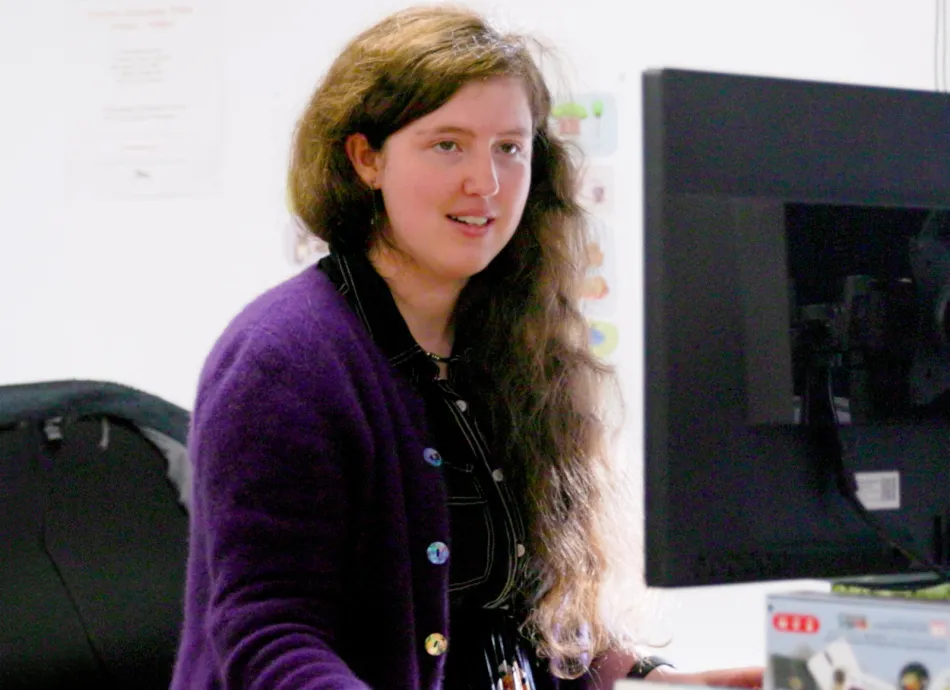 A woman with long hair smiling at her computer screen