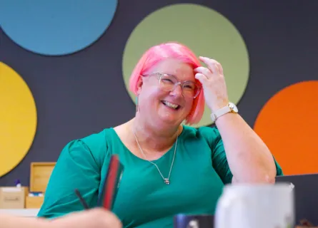 A woman with short pink hair and glasses smiling