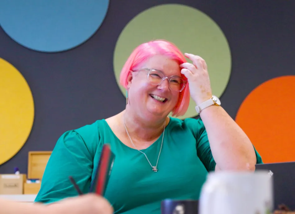 A woman with short pink hair and glasses smiling
