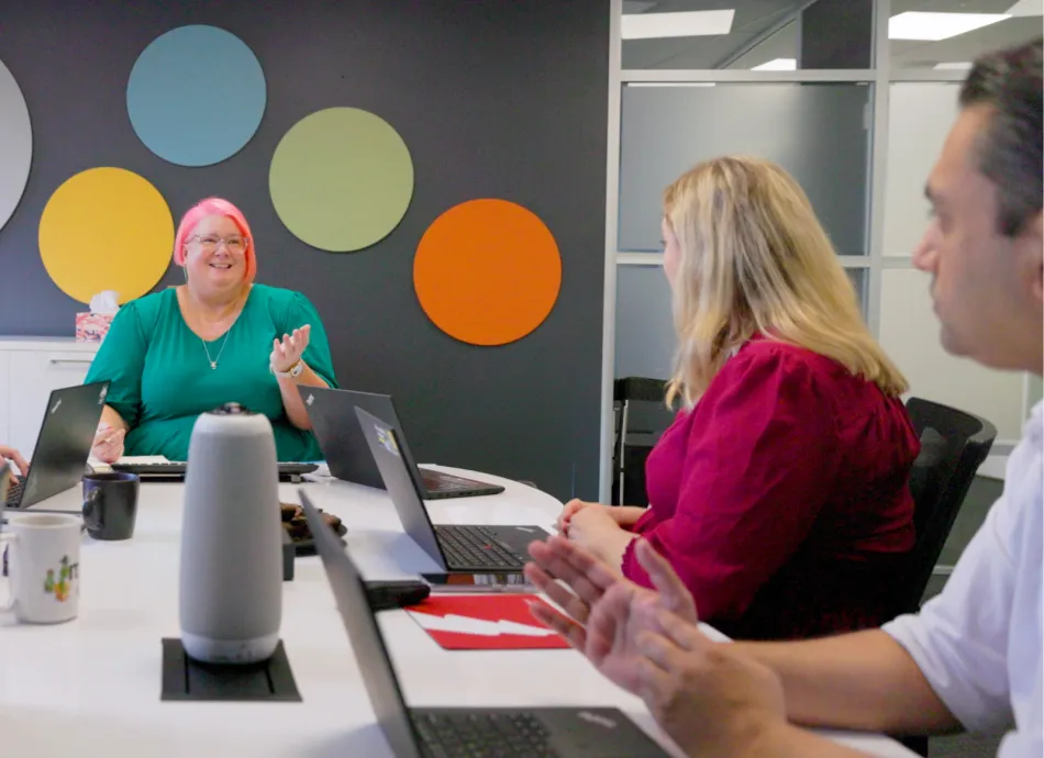 A woman with short pink hair talking to a woman and man in an board room setting