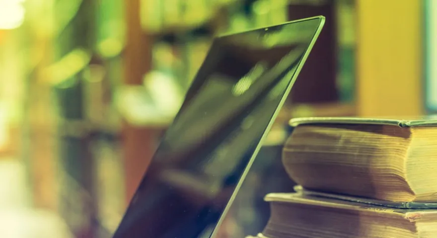 A laptop open next to a pile of books