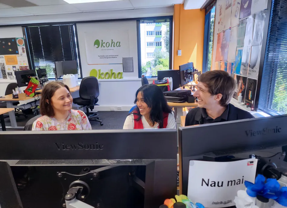 Wainui, Aleisha and Alex sit behind monitors and smile at each other as they work