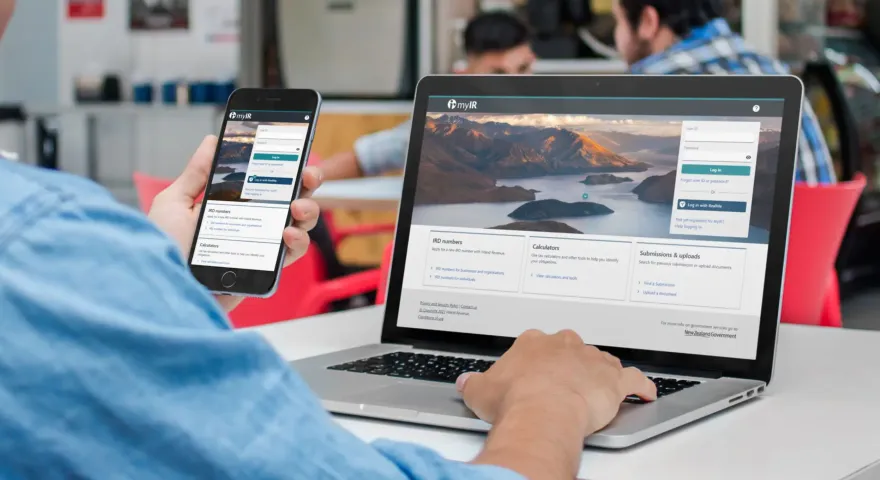 Person using a laptop and mobile device to navigate the home page of Inland Revenues website.