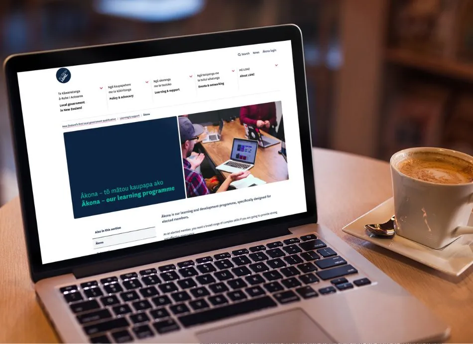 Open laptop displays the LGNZ website showing the landing page for Ākona, the digital learning platform for elected members. Next to the laptop is a flat white.
