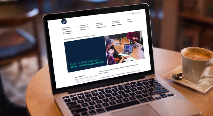 Open laptop displays the LGNZ website showing the landing page for Ākona, the digital learning platform for elected members. Next to the laptop is a flat white.