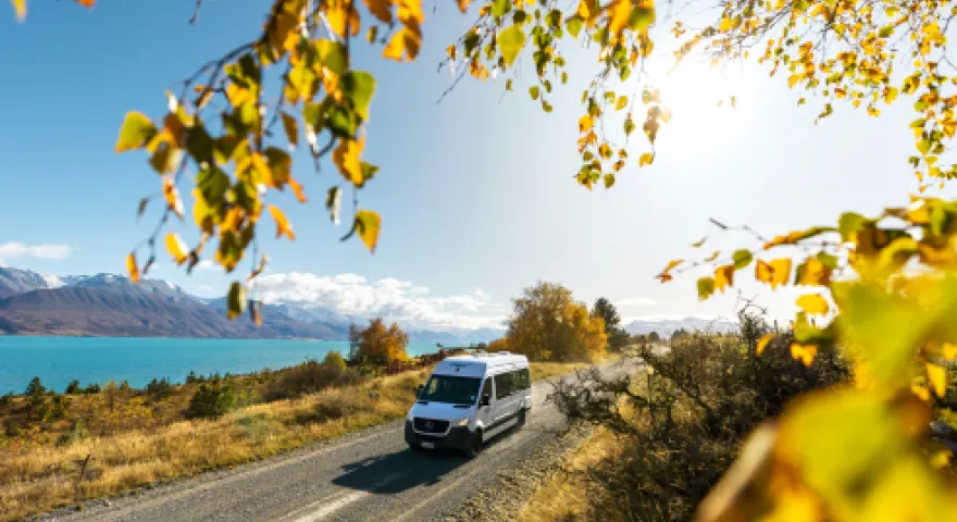 Van driving on an open road next to Lake Pukaki Canetebury. There are yellow leaves framing the van and it's a sunny day