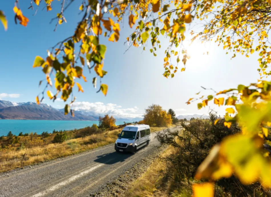 Van driving on an open road next to Lake Pukaki Canetebury. There are yellow leaves framing the van and it's a sunny day
