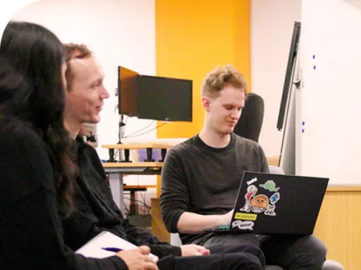 A man working on a laptop next to a man and woman in conversation
