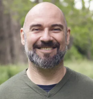 Smiling headshot of Ben Gardiner. He has a short beard and wears a green shirt.