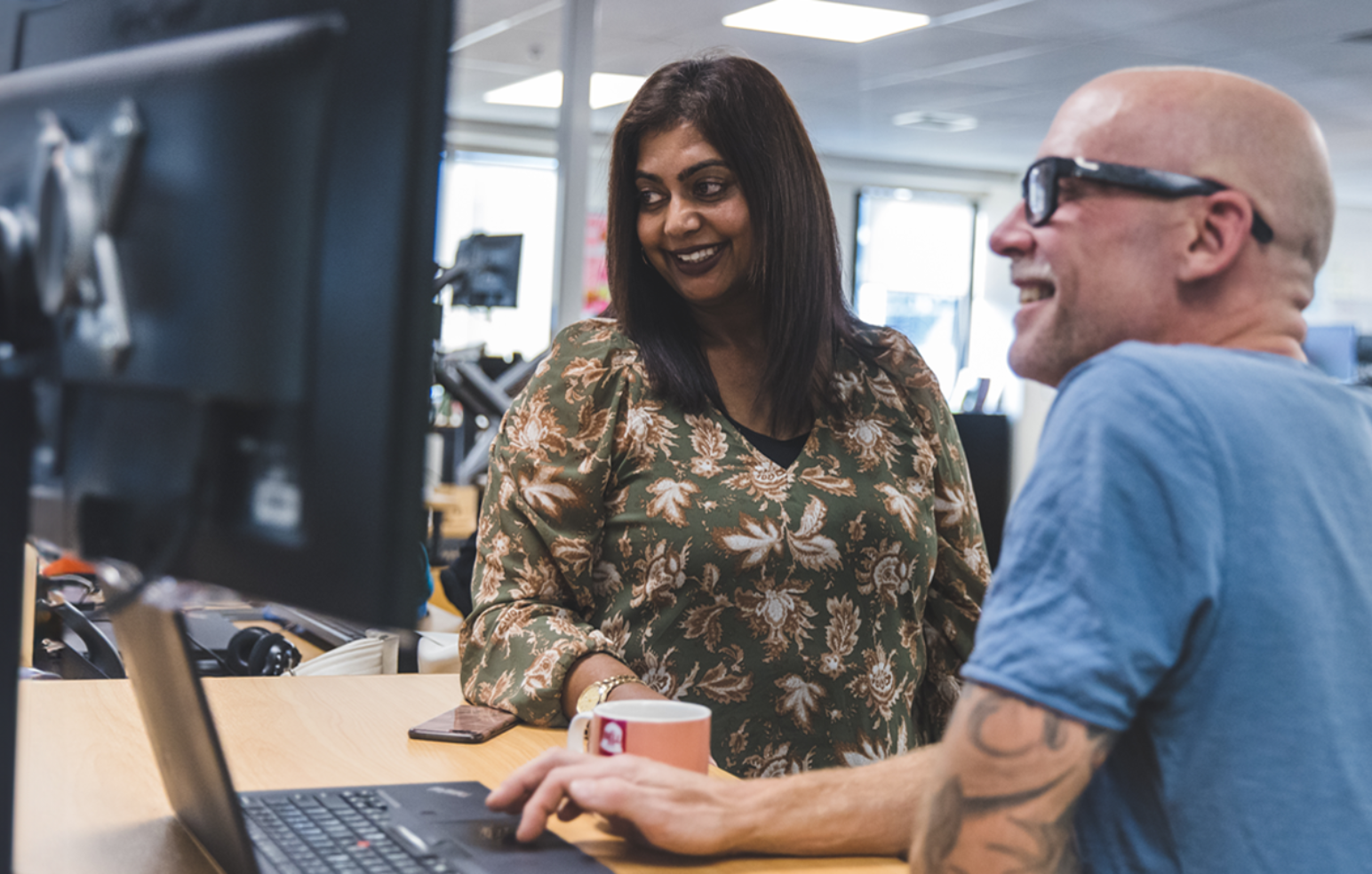 A man wearing glasses and woman with shoulder length black hair looking at a computer screen and smiling