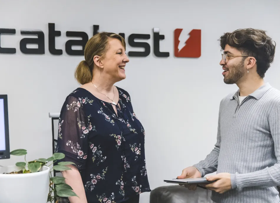 A man and woman smiling infront of a Catalyst wall sign