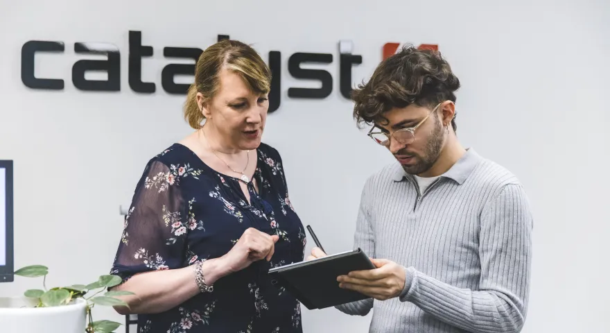 A man holding a tablet deveice and discussing the content on it with a woman stood next to him
