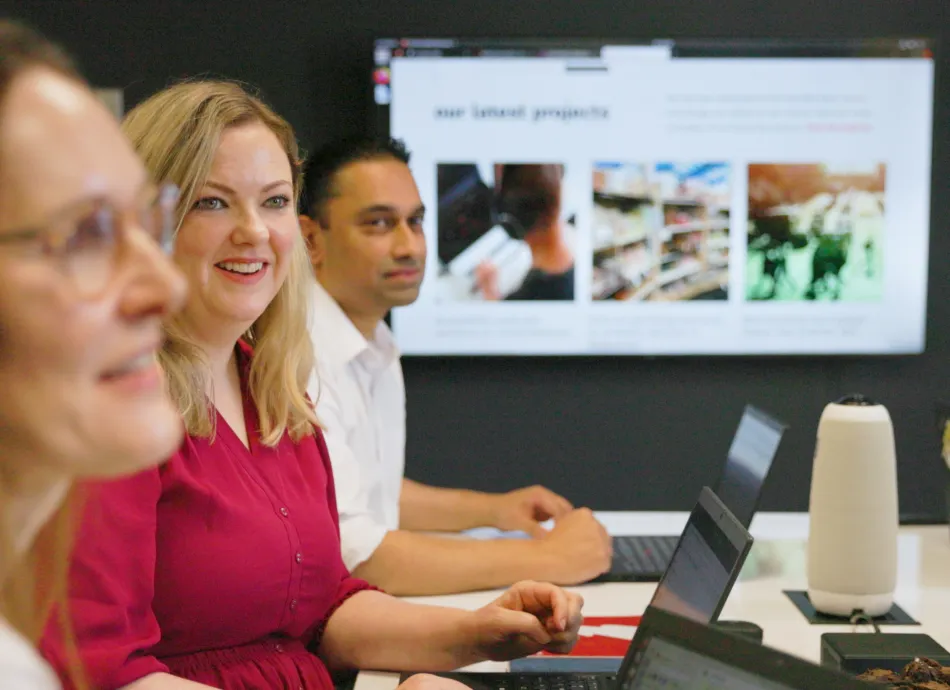 Two women and a man looking toward the camera with Catalyst case studies on a screen behind them