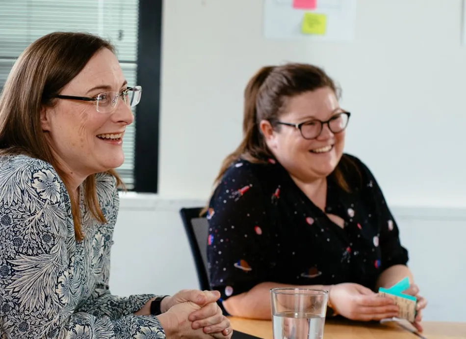 Two ladies from the Moodle team sit at a table smiling