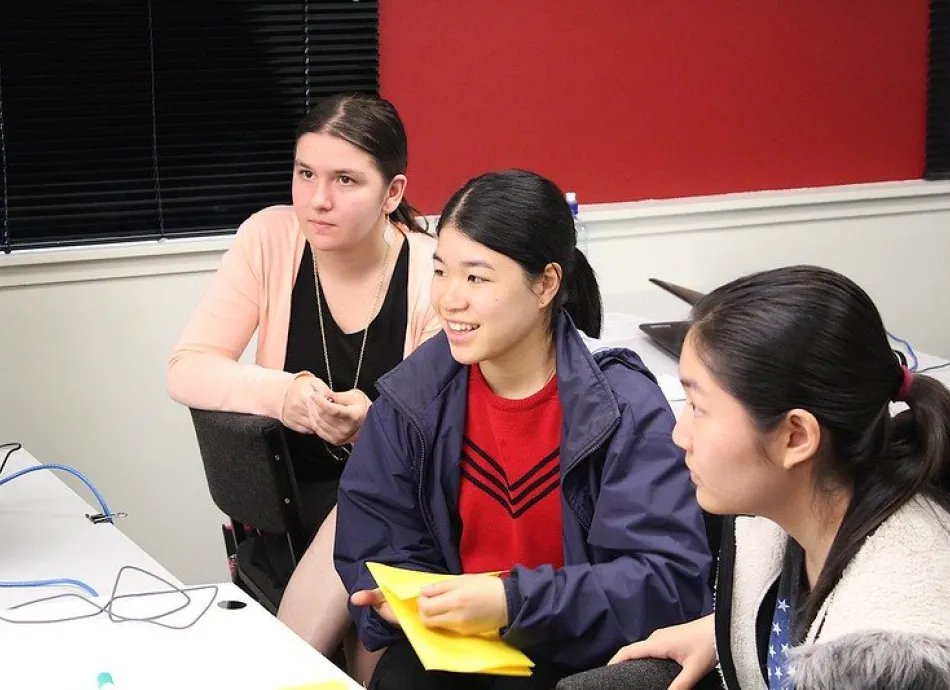 Three students are looking off camera towards a computer screen or instructor