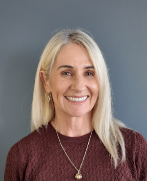 Smiling headshot of Anna Wilson. She has long blonde hair and wears a maroon shirt.