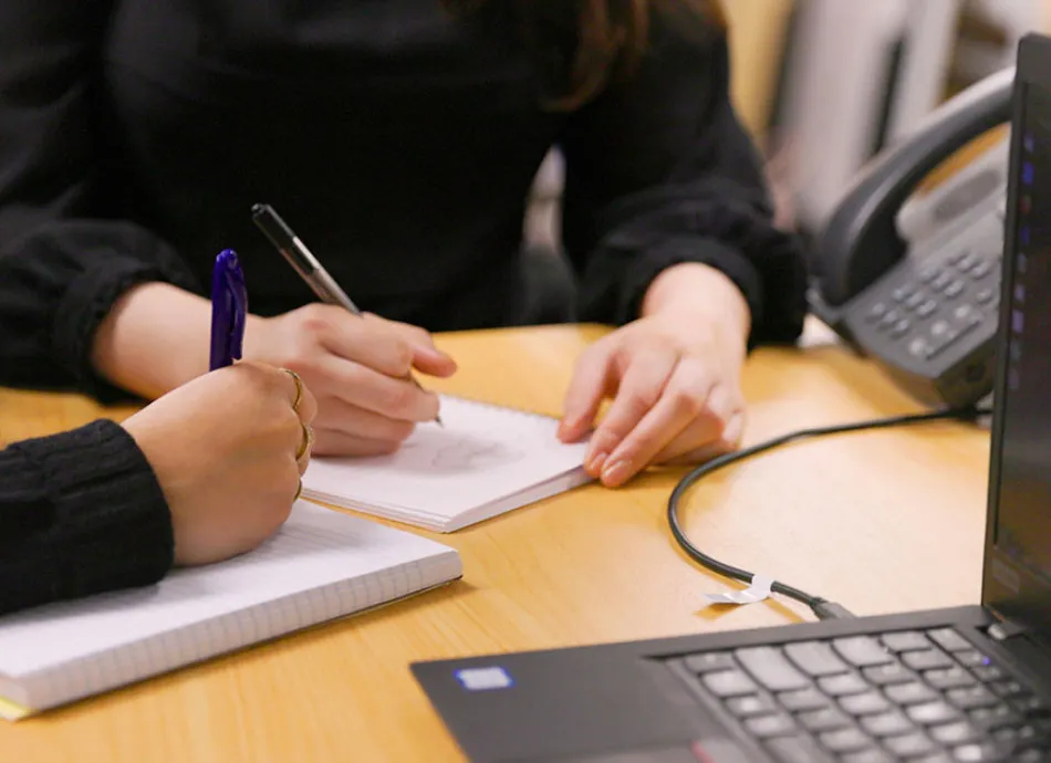 hands writing on notepads by laptop